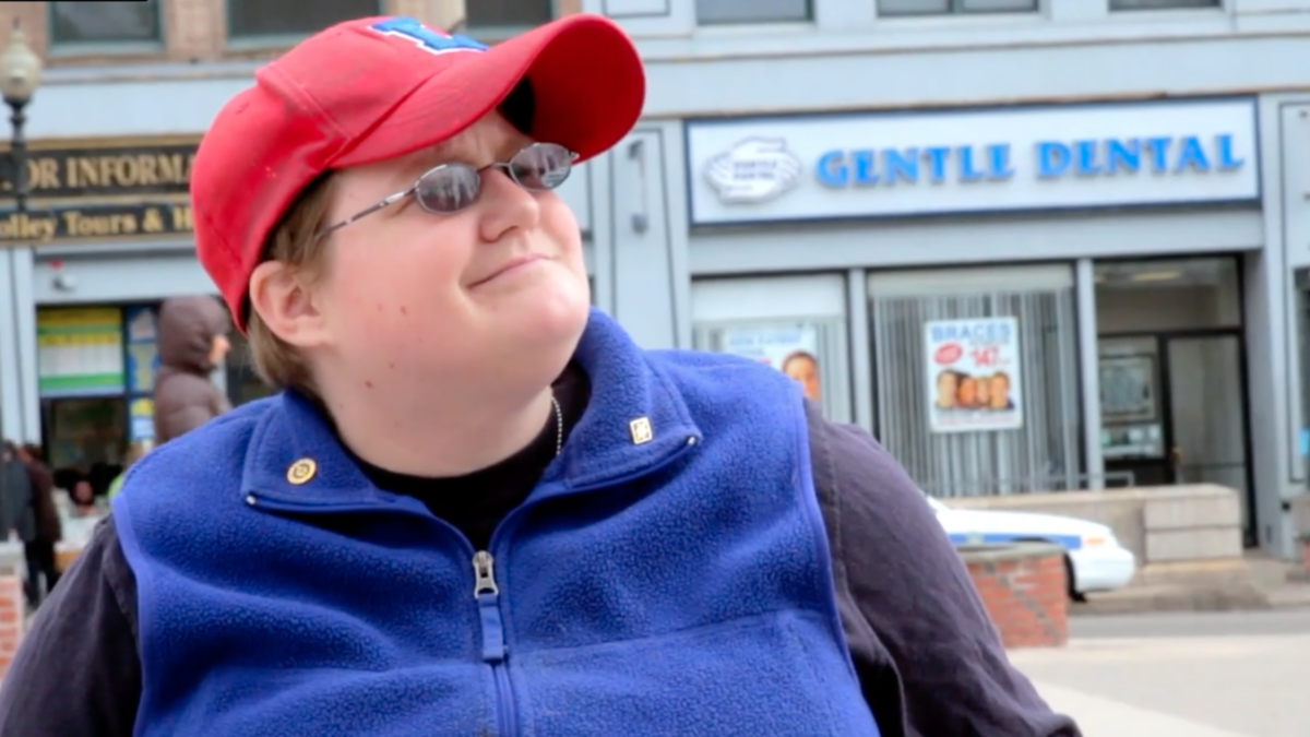 Olivia Richard wears a red cap, blue vest, and glasses.