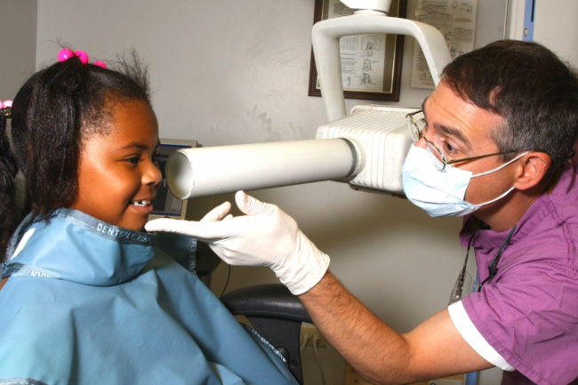 A child sits in a chair receives dental care from a dentist