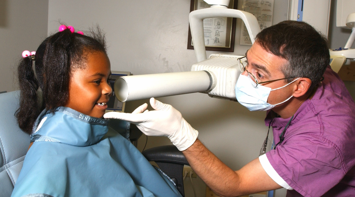 A child sits in a chair receives dental care from a dentist