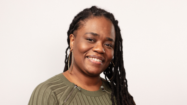 Dana Clarke, Senior Director of Operations and Management at Community Catalyst, wears an olive green sweater in front of a light background and is smiling directly at the camera.