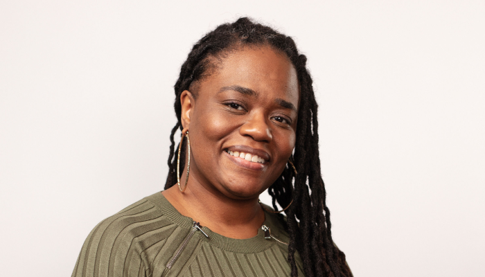 Dana Clarke, Senior Director of Operations and Management at Community Catalyst, wears an olive green sweater in front of a light background and is smiling directly at the camera.