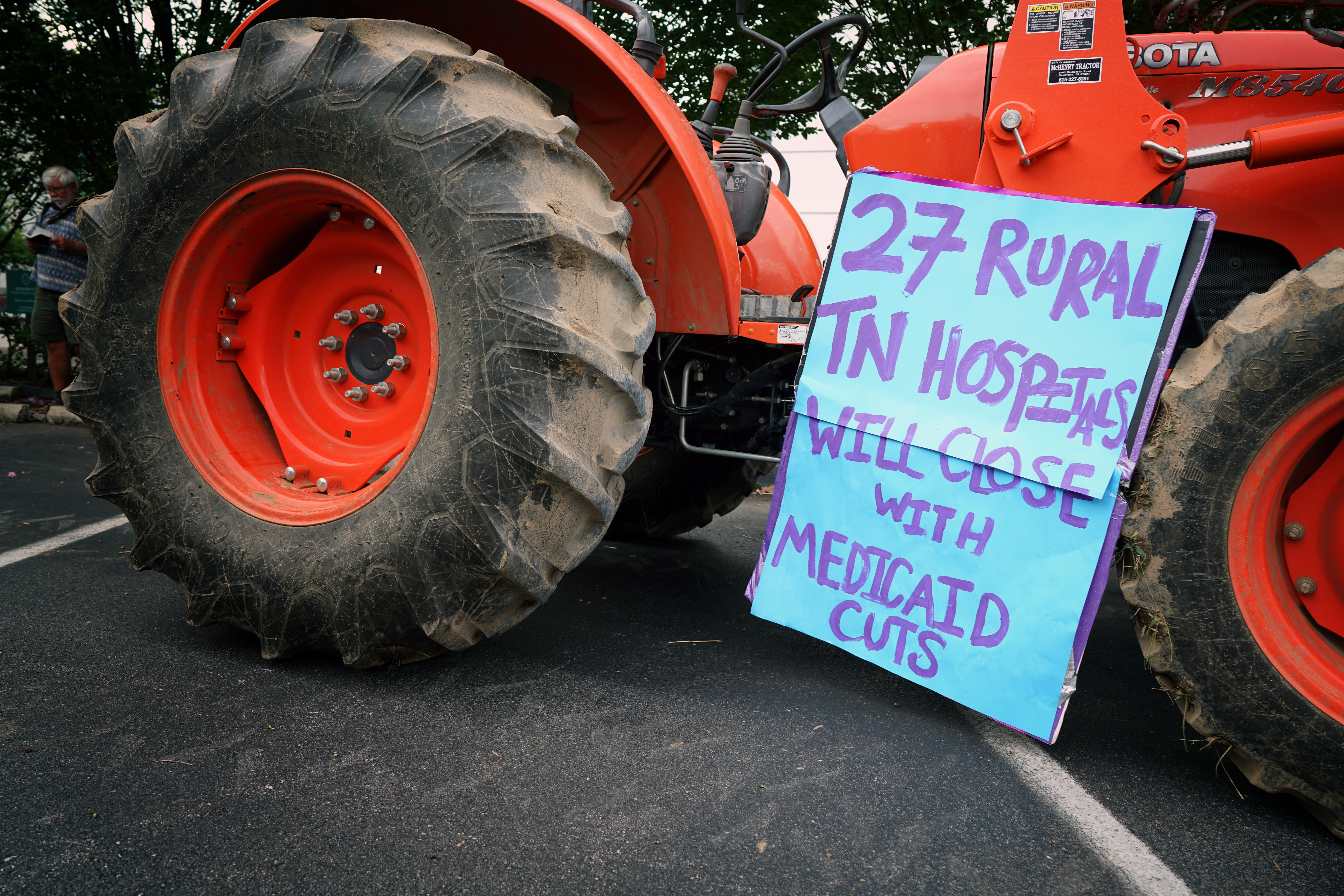 An orange tractor with a handmade poster leaning against it that says: "27 rural TN hospitals will close with Medicaid cuts"