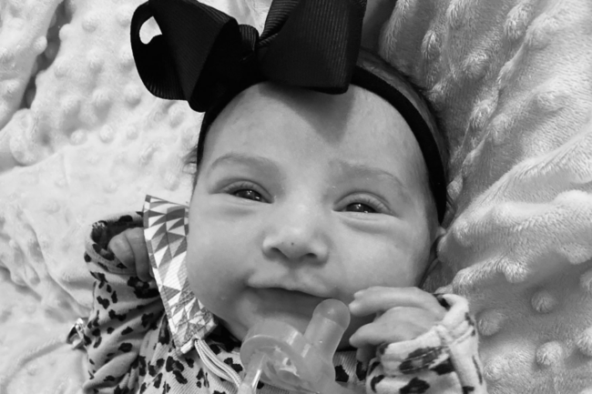 Black + white photo of baby with a pacifier close to her mouth