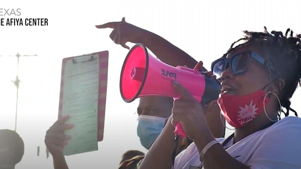 Woman with her hair in tight, short twists holds a bright pink megaphone and is presenting to a crowd