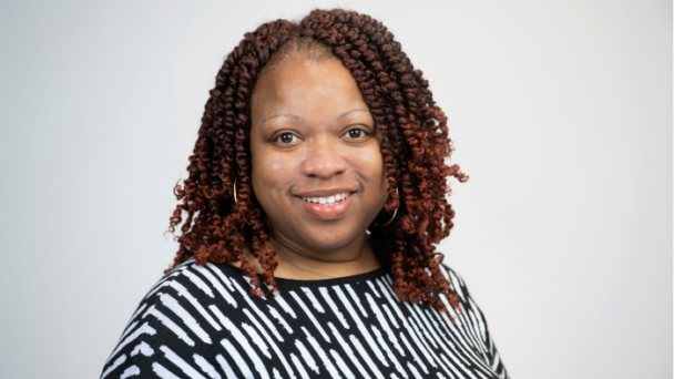 Traymanesha Lamy, senior director of programs and advocacy at Community Catalyst, smiles directly at the camera wearing a black and white top in front of a light background.
