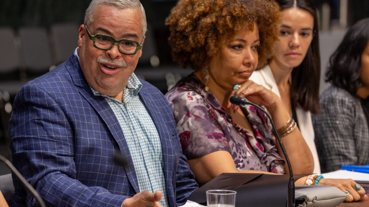 Man dressed in suit speaks into microphone with three people in the background at a roundtable of health advocates in Washington, D.C.