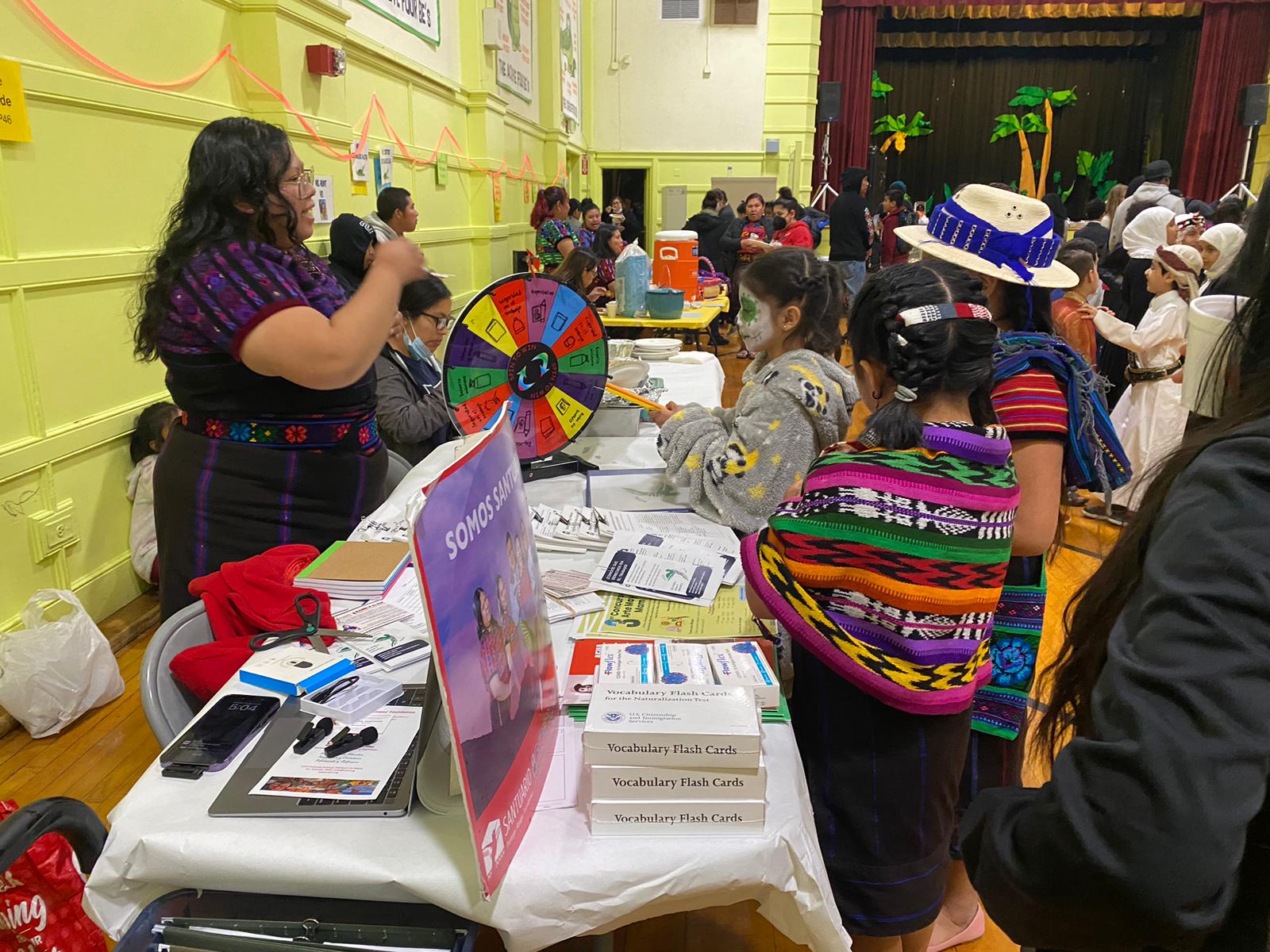 Two staff members of the Mayan Voices Outreach team share information about their programs to a group of children at an elementary school cultural event