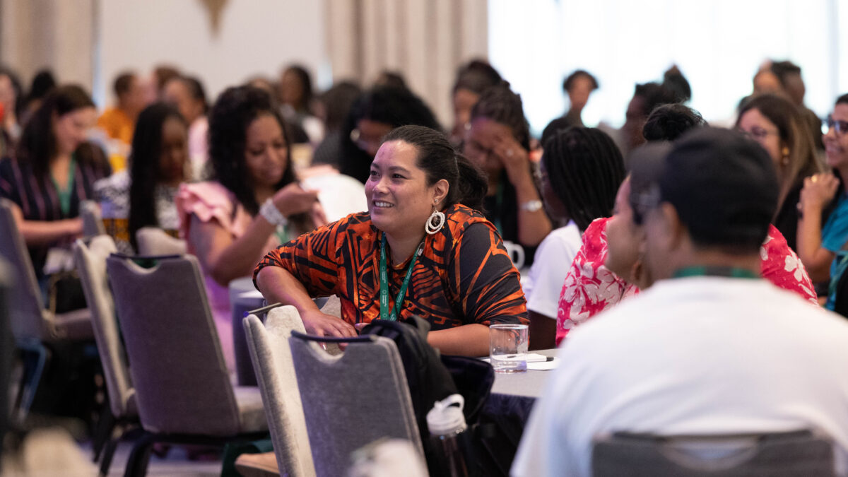 An attendee smiles while listening to a speaker in a packed conference room