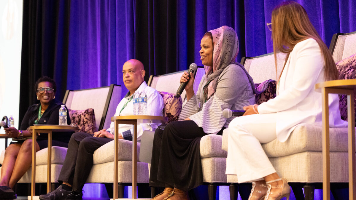 Four people sit in chairs and speak on a panel about health equity