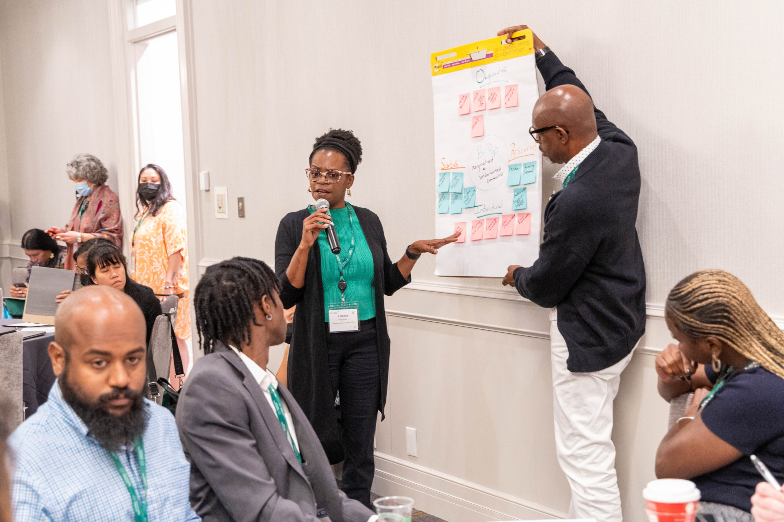 Two people share information on a poster to a breakout group of health advocates as part of the 2023 Vaccine Equity and Access Conference
