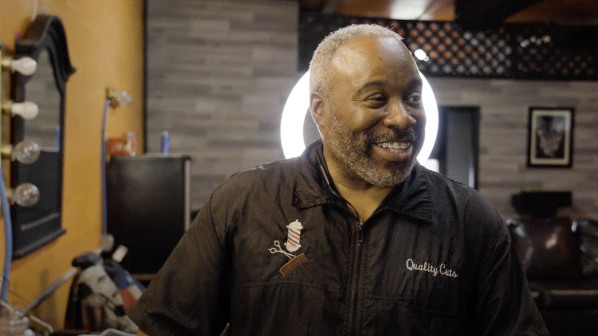 A barber smiles and poses in a barbershop.