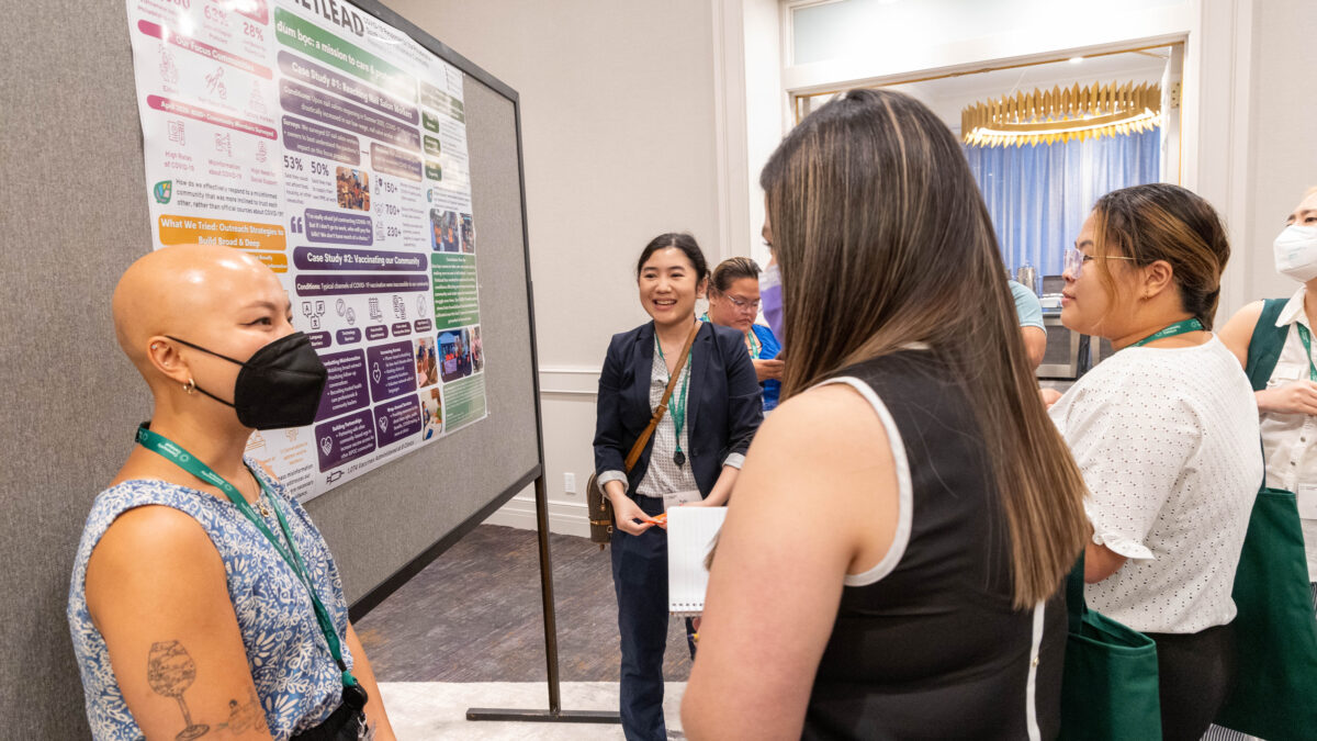 Two people share information on a poster to a breakout group of health advocates as part of the 2023 Vaccine Equity and Access Conference