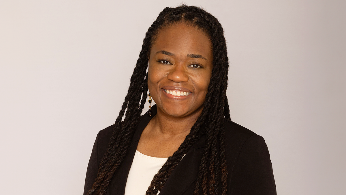 This portrait features a woman smiling with long twists and wearing a black blazer and white shirt.