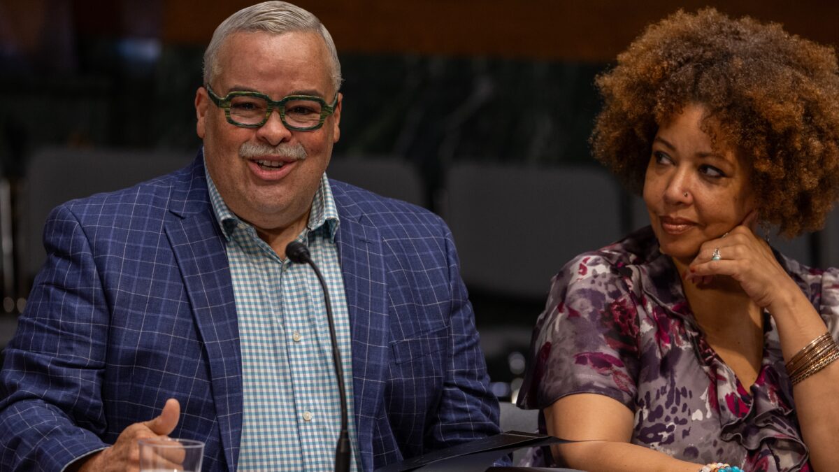 Man dressed in suit and a woman in a multicolored shirt speak at a table in Washington, D.C.