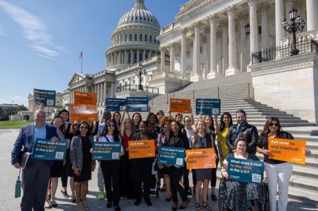 A large group of community members and advocates hold signs and pose in front of the steps of the U.S. Capitol in Washington, D.C.