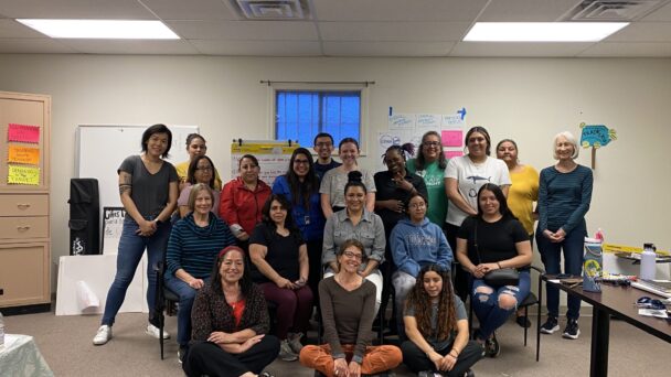 Twenty people smile and pose for a photo in an office meeting room