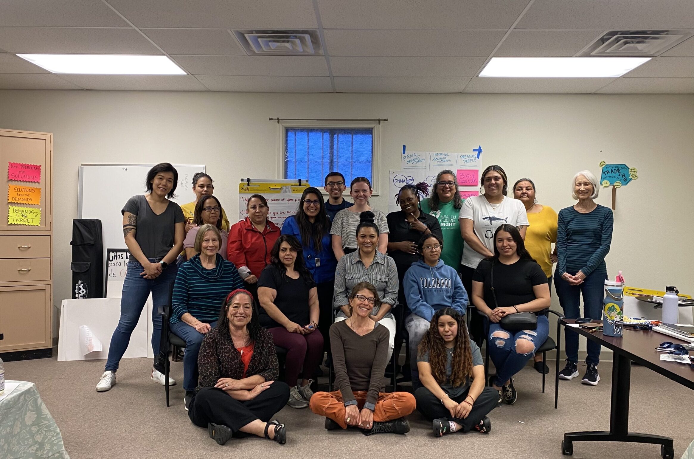 Twenty people smile and pose for a photo in an office meeting room