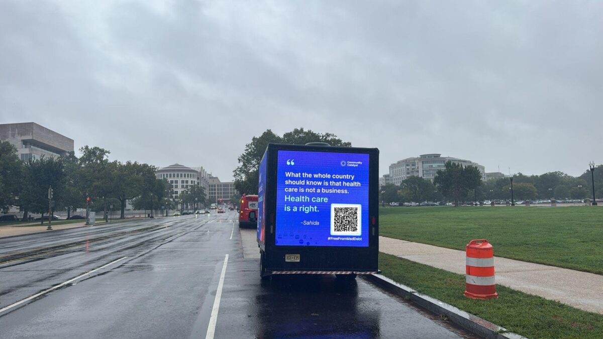 A mobile billboard is parked on a tree-lined road in Washington, D.C. that reads "What the whole country should know is that health care is not a business. Health care is a right."