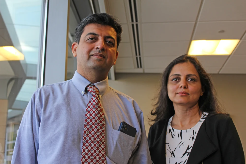 A man wearing a red tie and blue shirt and a woman wearing a black blazer and white and black blouse pose for a photo in an office.