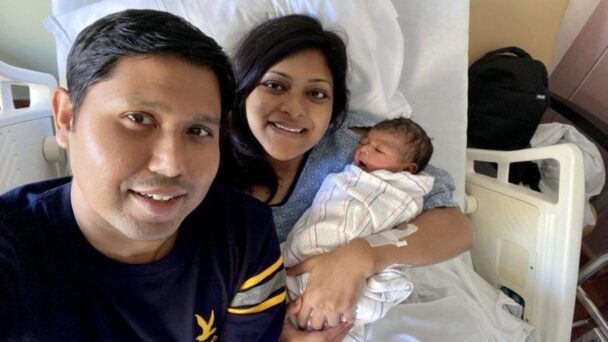 Two parents smile and hold their newborn child at the hospital