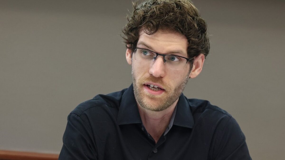 Jason speaks in a conference room. He is wearing glasses and a black shirt.