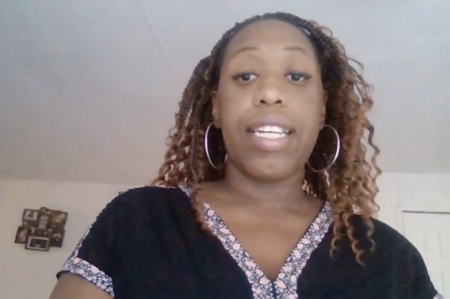 Sherthea has brown curly braids and is wearing earrings and a black and pink blouse.