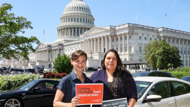 Two people pose in front of the Capitol in Washington, D.C. They are holding signs that read, "Cutting Medicaid fuels medical debt" and "We're done paying the price."