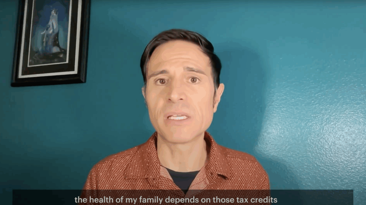Ricky speaks in front of a blue wall and a framed painting. He has brown hair and is wearing an orange shirt. The caption reads: "The health of my family depends on those tax credits."