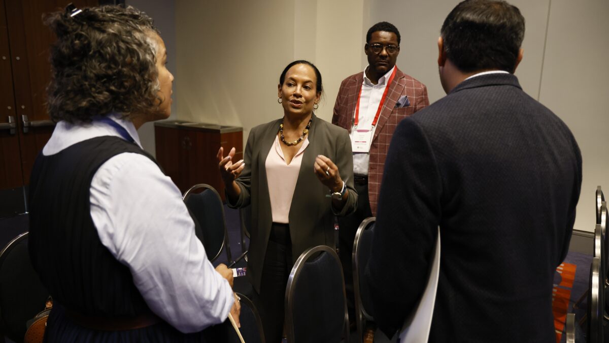Community Catalyst President & CEO Linda Goler Bloun speaks with two people in a conference room. Another person in a red suit is standing behind her.