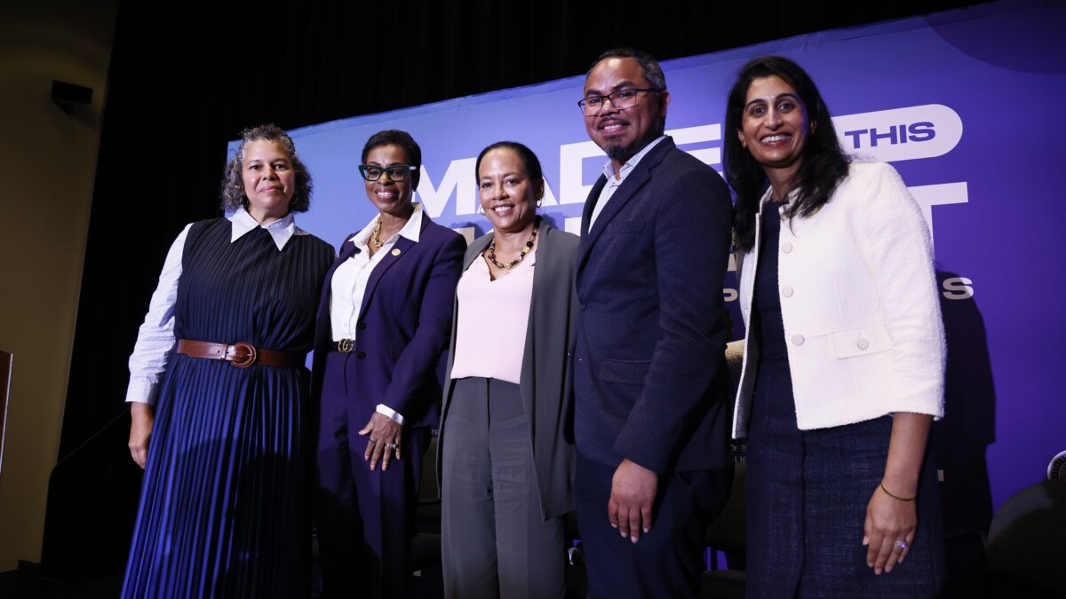 Five panelists stand and pose in front of a purple sign that says "Made for this moment. Power, Policy, & Progress."
