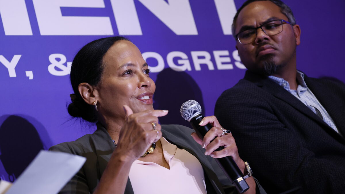 Community Catalyst President & CEO Linda Goler Blount speaks into a microphone in front of a purple wall.